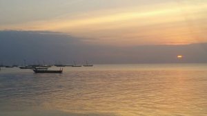 Die Sonne geht im Meer unter auf Sansibar, im Vordergrund kleinere Boote